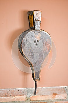 close up of an old bellows made in leather and wood. The bellows in vertical position is rested on a wall of bricks and an a brown