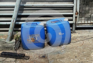 Close up of an old blue plastic gallon of oil on the ground beside a metal fence