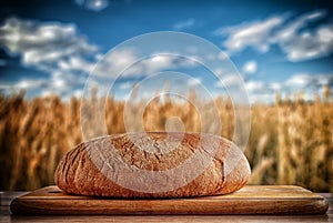 Close-up on an old brown table, a man cuts a round dark bread on a wooden board against a dark background