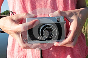 Close-up of old camera in hands. Young woman in pink t-shirt holding vintage film camera.