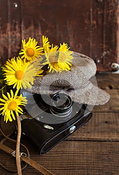 Close up of an old camera vintage hat and a bouquet of yellow flowers on a wooden background