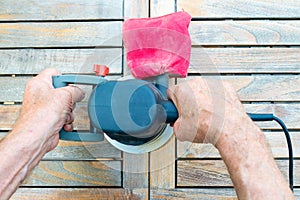 Close-up of old carpenter`s hands working with electric sander