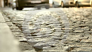 Close up of an old cobblestone road and cars passing in a distance. Abstract vintage street background.