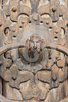 Close-up of an old decorated, corroded, rusty door knocker in the shape of a human head