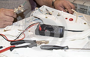 Close-up of the old electrician`s hand, the use of digital voltmeter for voltage to repair the electric iron, selective
