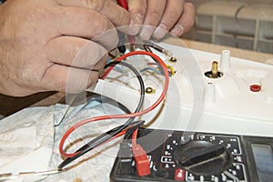 Close-up of the old electrician`s hand, the use of digital voltmeter for voltage to repair the electric iron, selective