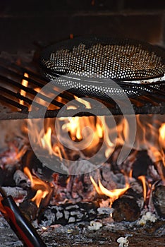 Close up of old-fashioned popcorn popper over flaming grill
