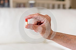 Close up of old female hand holding a red and white capsule pill in two fingers. Health care concept