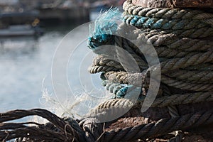 Close up of old, frayed rope tethering fishing boat to mooring in the harbor