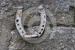 Close up of an old gray rusted horseshoe hanging on the stone wall. Antique rust horse shoe on the concrete texture with cracks