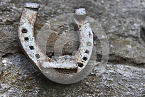 Close up of an old gray rusted horseshoe hanging on the stone wall. Antique rust horse shoe on the concrete texture with cracks