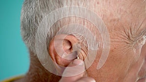 Close-up of old man cleaning dirty ears with cotton swab. Ear cleaning and care