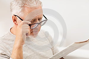 Close up of old man in glasses reading newspaper