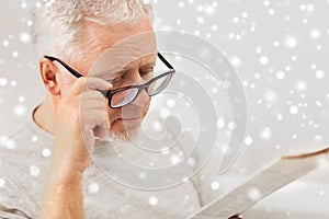 Close up of old man in glasses reading newspaper