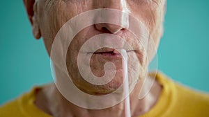 Close-up of an old man greedily drinking juice or cocktail from a straw