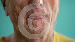 Close-up of old man licking his lips on blue background. Body parts