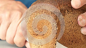 Close-up of an old man`s hand cutting a piece of black bread. The elderly person is starving and in need. Delicious lunch with fre