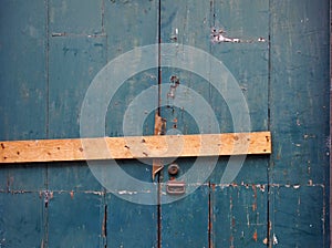 close up of an old peeling green painted wooden plank door barred shut with a piece of timber and rusty nails with a lock and