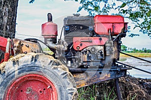 Close up of the old red tiller tractor or walking tractor parked under the tree in the fields at countryside, Thailand