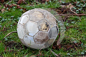 Close up of old rough looking football left out in all weathers on untidy grass