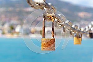 Close up of old rusty locks on chain against background of city and sea. Blurred backgroud