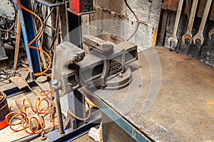 Close-up of an old rusty vise in the garage. A table in the workshop on which the clamp stands. Wrenches over the table