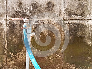 Close up old stainless steel Faucets and blue water rubber hoses on dirty rough cement wall with copy space