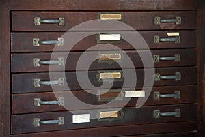 Close up of old vintage vertical wooden cabinet with drawer, handles, plates and blank weathered label for documents.