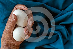 Close-up of the old woman's hand Poor Thai grandmother holds a large white duck egg for dinner. Pure egg whites