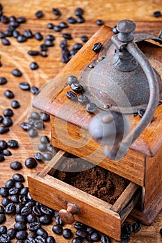 Close-up of old wooden coffee grinder with ground coffee in drawer, and coffee beans on wooden table