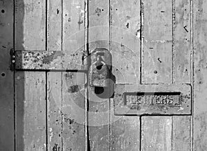 Close up of an old wooden door with cracked faded paint and a rusty closed padlock and old metal letterbox