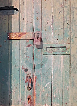 close up of an old wooden door with green faded paint and a rusty closed padlock and old metal letterbox