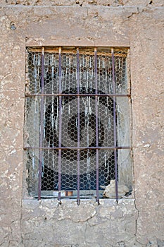 close up of an old wooden window with bars of iron blocking the access, in a wall of concrete, mud and stone in a closed abandoned