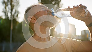 Close up older man drinking clear mineral water morning sun rays thirsty male drink pure aqua bottle city sunlight