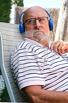 Closeup of a retired senior man looking to the side wearing blue headphones sitting on a lawn chair