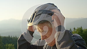 CLOSE UP: Older man puts on a helmet before a bicycle ride on a sunny evening.