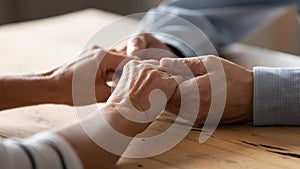 Close up older spouses holding hands on wooden table photo