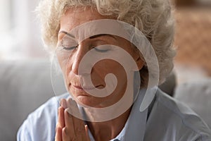 Close up older woman with closed eyes praying with hope