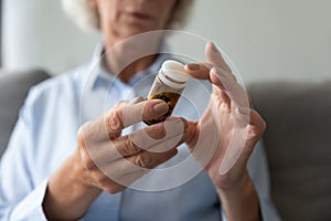Close up older woman holding bottle with pills, reading instruction
