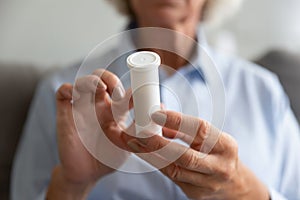 Close up older woman holding white plastic bottle with pills