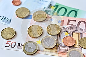 Close up of one euro coin surrounded by different coins and 100 and 50 Euro banknotes