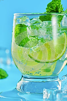 Close-up of one glass with a mojito cocktail on a blue background. Vertical shot from a low angle