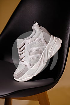 Close up of one white sneaker standing leaning on back of black chair in studio.