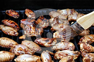 Close up of an open barbecue grill cooking chicken wings while being brushed with sauce