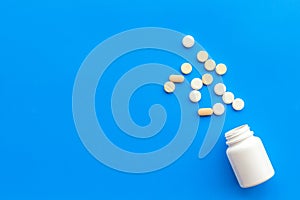 Close up of an open bottle of medicine and its lid. Several pills are lying on blue desk. Pharmacology and medical photo