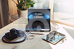 Close-up of open laptop with inscription on monitor- cloud library on wooden table. Nearby is a tablet computer, camera, notepad