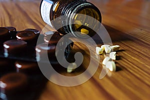 Close up Open transparent glass bottle with medicine pills or tablets blister pack on wooden table background. Pharmacy cure and