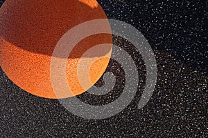 Close up of orange color grain textured stone ball on the left on black asphalt background. Full frame. Reidi tee street