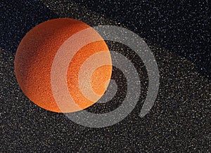 Close up of orange color grain textured stone ball on the left on black asphalt background. Full frame. Reidi tee street