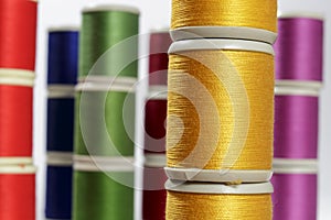 Close-up orange cotton thread bobbins. Other color threads in background